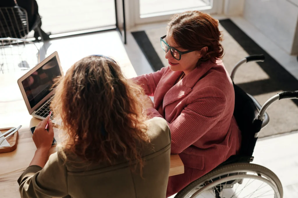 a woman in a wheelchair looking at her laptop with a business partner