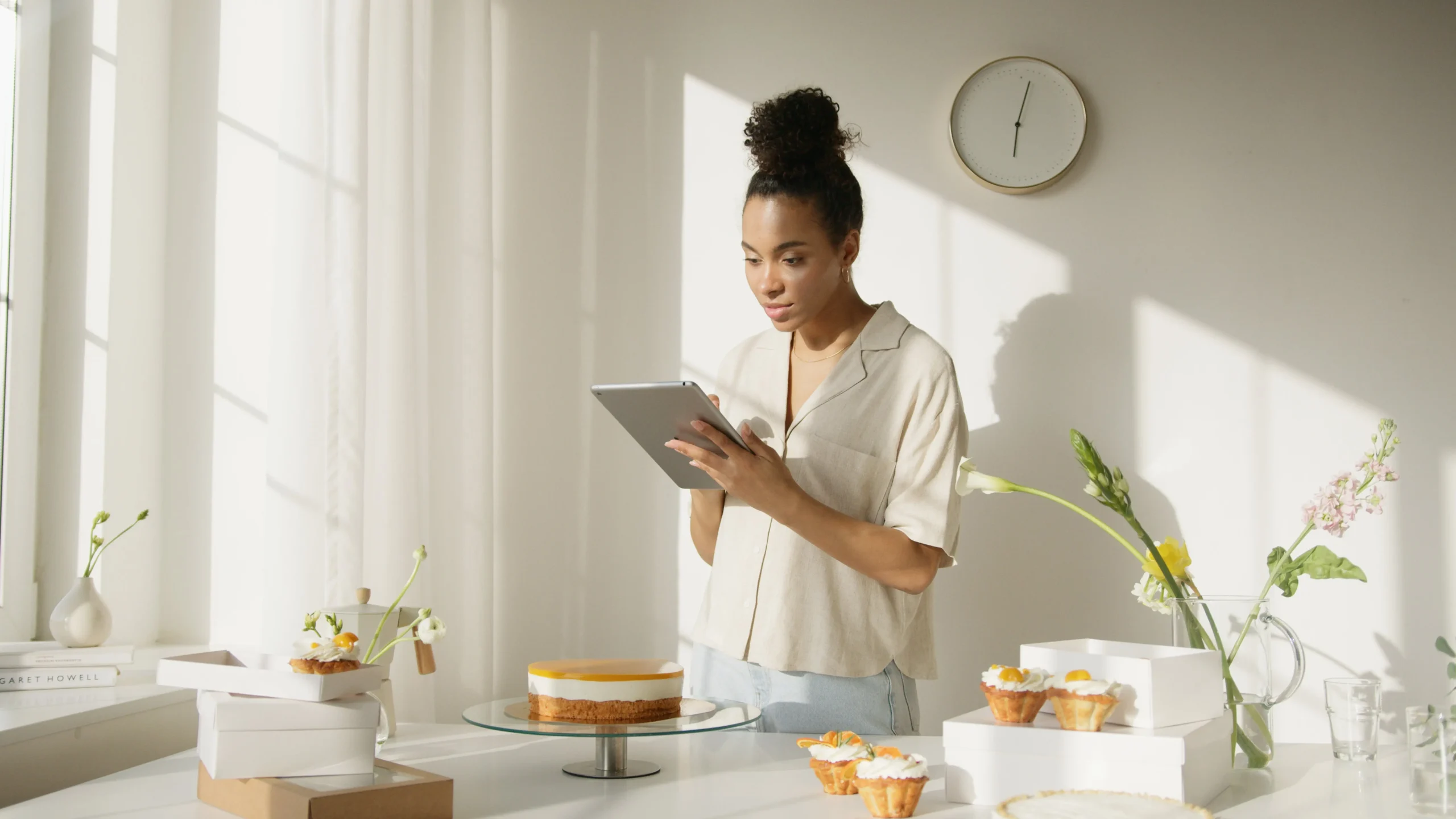 a Black woman looking at her tablet with cakes on the table