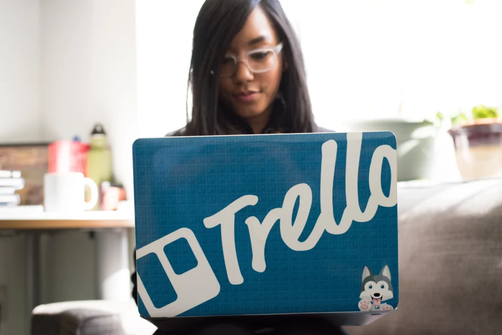 a woman working on a laptop with the trello logo on it
